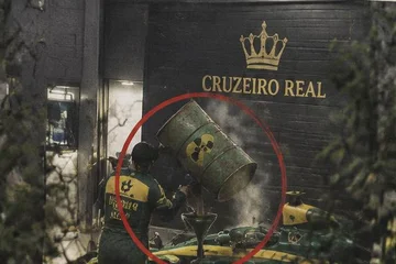 Foto granulada: diante da garagem, um homem vira um tambor com o símbolo de radioatividade num funil encaixado no carro de corrida.