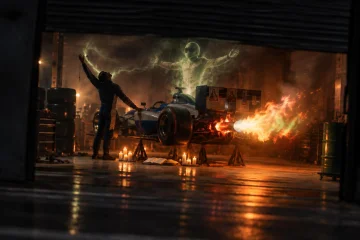 Um carro de corrida da Cruzeiro Real, erguido em cavaletes, cospe fogo pelo escapamento enquanto alguém, contra a luz, o abençoa em êxtase, e um piloto-fantasma verde sobe do motor.